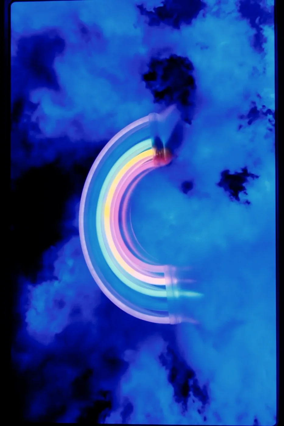 A neon rainbow blurred by a long exposure against blue-lit clouds